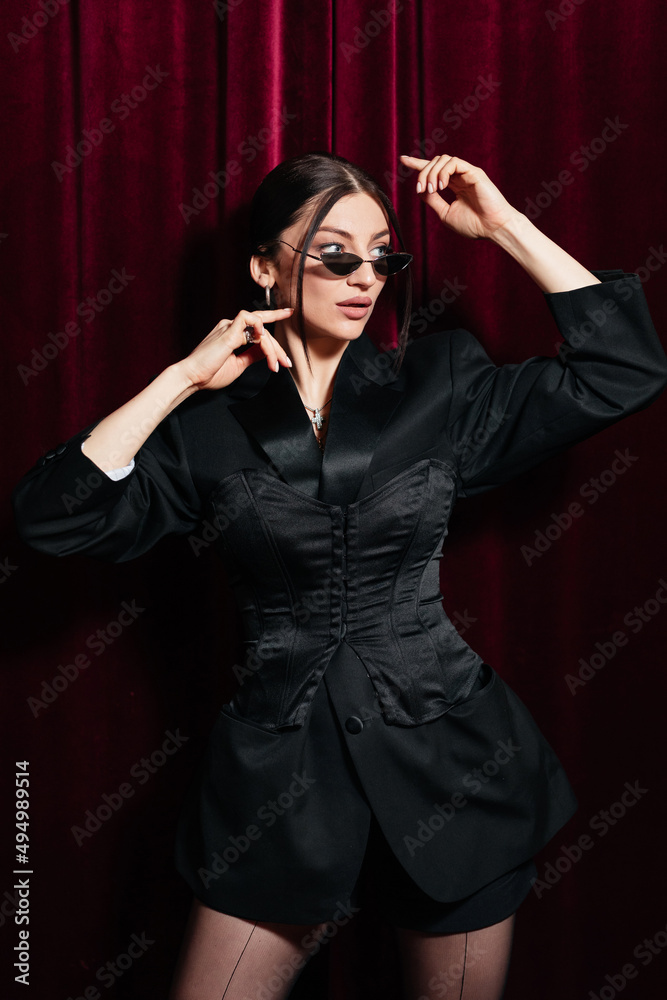 A model wearing all black posing in front of a red cinema curtain A model wearing all black posing in front of a red cinema curtain