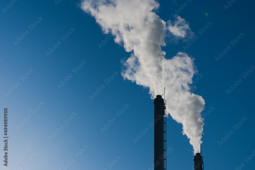 factory pipes against the blue sky. white smoke comes out of metal pipes.