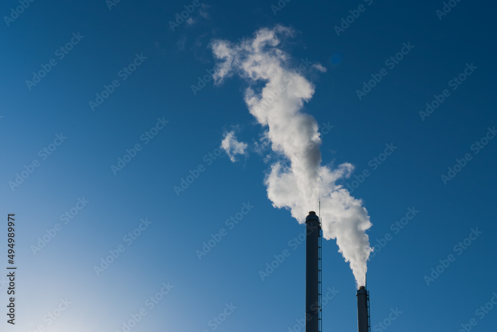 factory pipes against the blue sky. white smoke comes out of metal pipes. factory pipes against the blue sky. white smoke comes out of metal pipes.