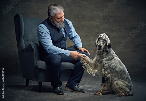 Old man shaking paw of his dog sitting on armchair