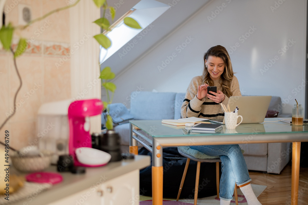 Woman using smartphone while working at home and using a laptop Woman using smartphone while working at home and using a laptop