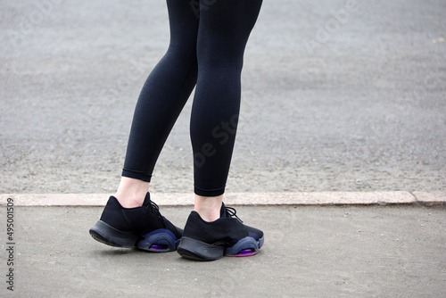 Female legs in sneakers and leggings on asphalt, slim girl runner on a street. Concept of spring workout in city
