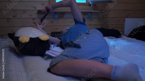 the boy is lying on the mattress and playing with the phone. esports on a tablet. he looks at the screen