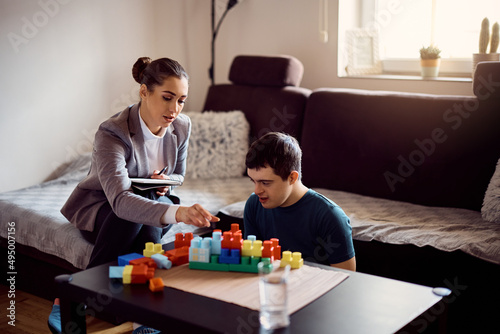 Young psychologist stacking toy blocks with down syndrome man during home visit.