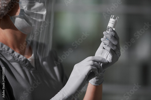Close-up shot of unrecognizable modern doctor wearing personal protection equipment filling syringe with Covid-19 vaccine, copy space