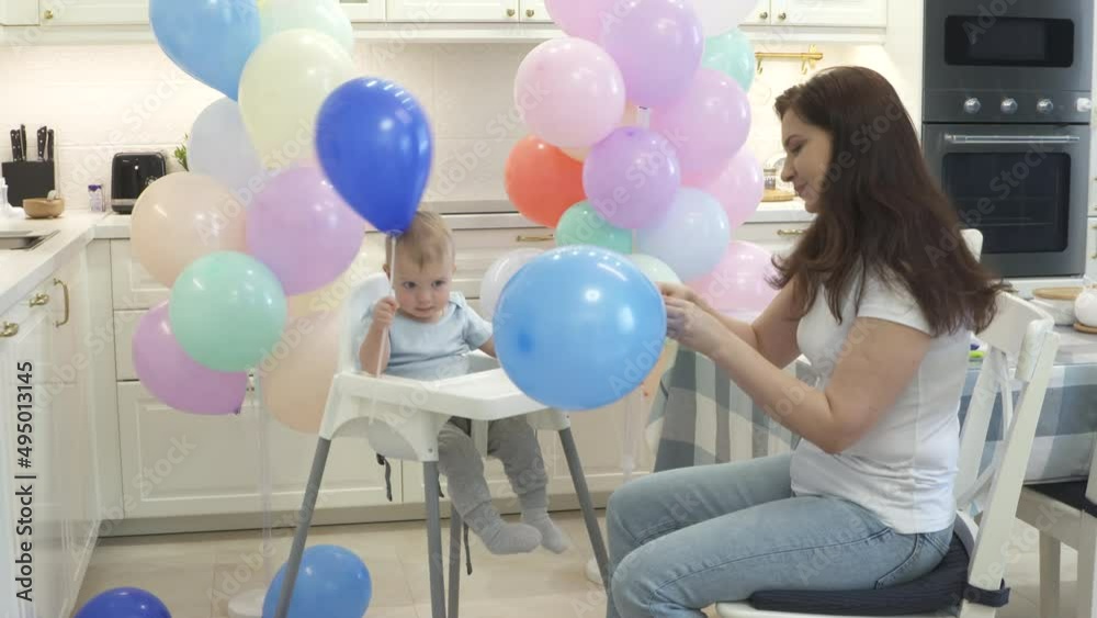 Mother and baby are preparing to celebrate children birthday blowing up balloons to decorate home for party. High quality 4k footage