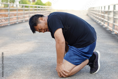 Asian man runner fell down on the floor, feels hurt. Concept : injury knee twist sprain accident in workout or sport. Health problems. Copy space for text. 