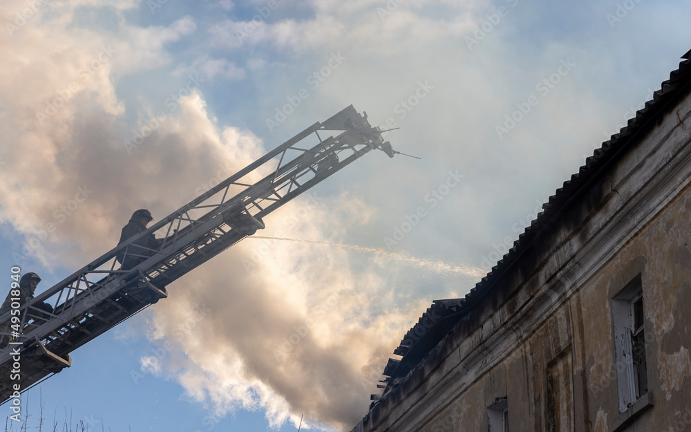 Firefighter pours water on fire. Rescue services during work. Extinguishing fire from hydrant. Firefighter on retractable ladder.