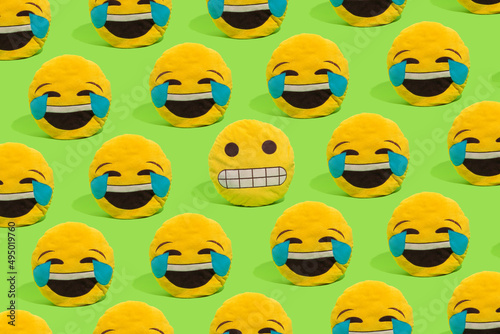 Scheme of yellow smiley pillows laughing at a smiley with a embarrassed grimace on a green background. photo