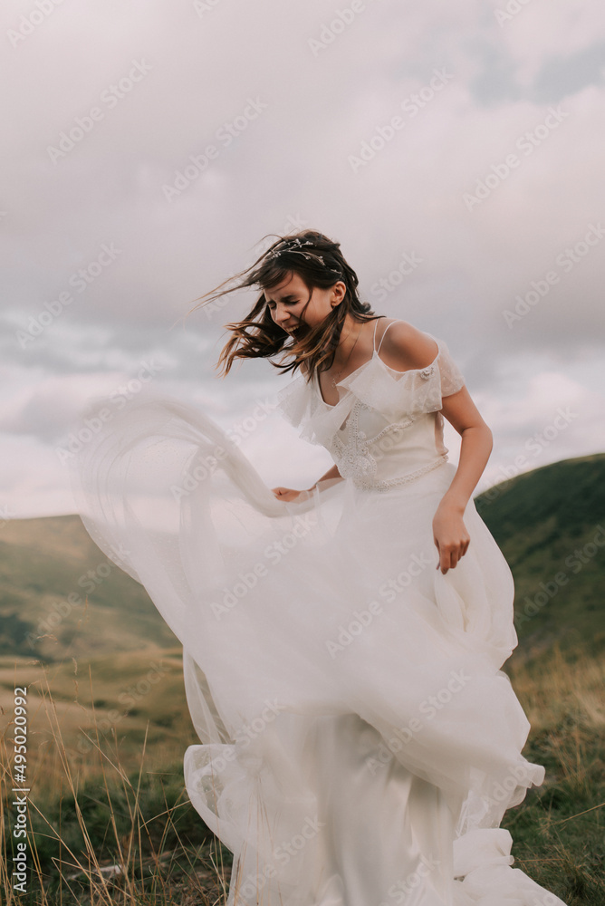 Happy bride in white wedding dress smiling against the backdrop of mountains.
