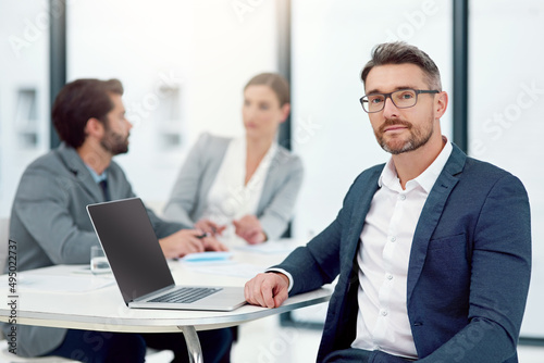 Were all about inspiring innovation. Portrait of a businessman sitting in a boardroom meeting with colleagues in the background.