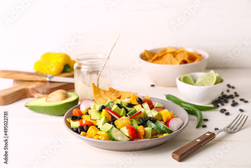 Bowl of tasty Mexican salad with black beans and radish on light wooden table