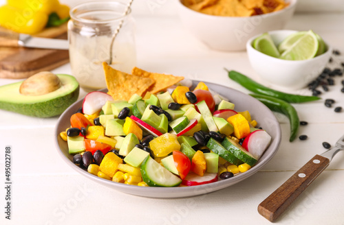 Bowl of tasty Mexican salad with black beans and radish on light wooden table