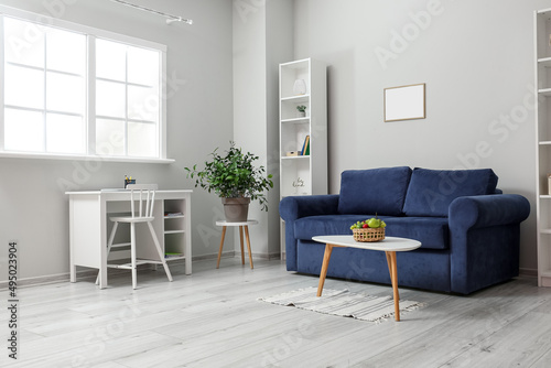 Interior of light living room with blue sofa, table and fruit basket