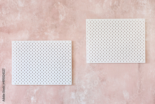 Stylish white peg board hanging on textured pink wall