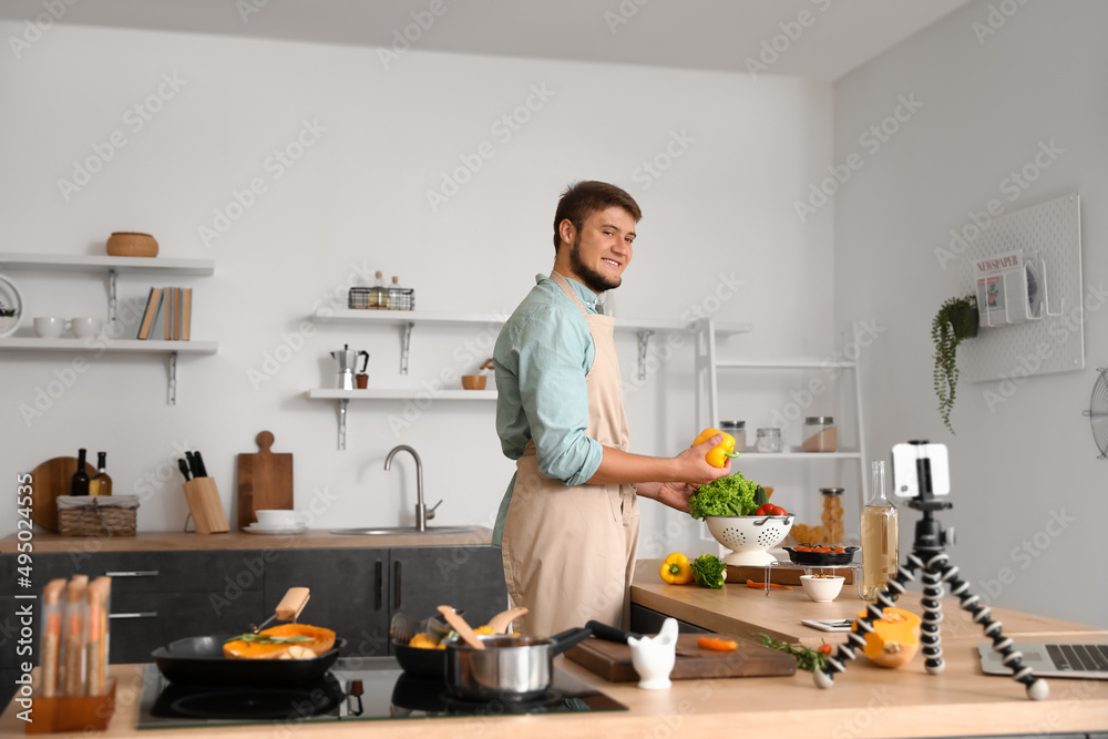 Young man with vegetables recording cooking video tutorial in kitchen Young man with vegetables recording cooking video tutorial in kitchen