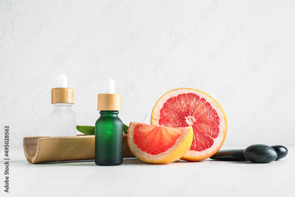 Composition with bottles of essential oil and grapefruit on light background Composition with bottles of essential oil and grapefruit on light background