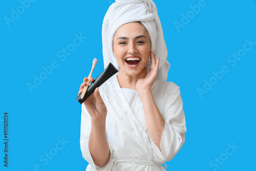 Beautiful young woman in bathrobe, with activated charcoal tooth paste and brush on blue background © Pixel-Shot