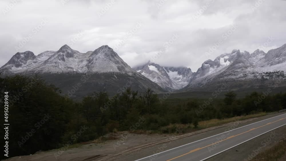View of the road in the woods. We can see cars and trucks passing by and the Andes mountains in the background. Shot made in Ushuaia, Tierra del Fuego, Patagonia Argentina. View of the road in the woods. We can see cars and trucks passing by and the Andes mountains in the background. Shot made in Ushuaia, Tierra del Fuego, Patagonia Argentina.