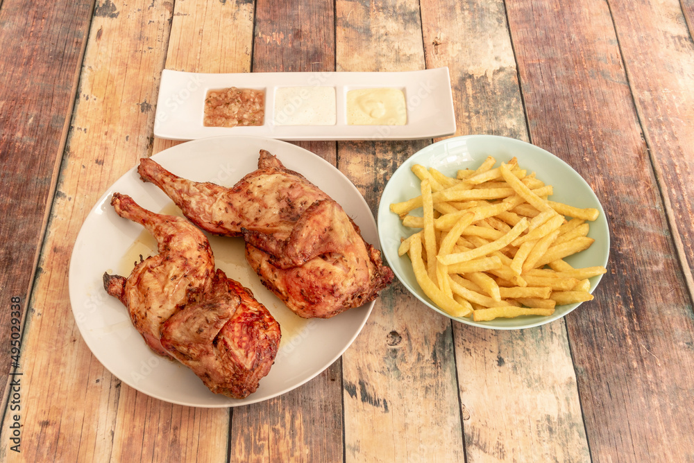 Grilled chicken cut in half with french fries and sauces on wooden table Grilled chicken cut in half with french fries and sauces on wooden table
