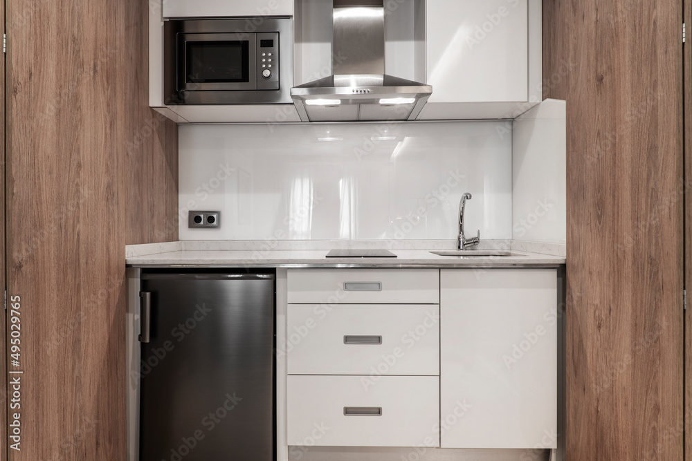 Photo of a kitchen front with wooden doors and a small glossy gray fridge. Photo of a kitchen front with wooden doors and a small glossy gray fridge.