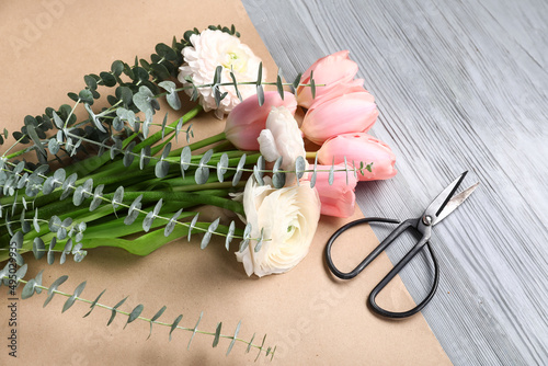 Beautiful flowers, wrapping paper and scissors on grey wooden background