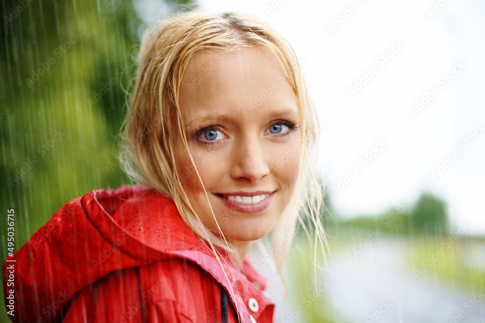 Gorgeous young blonde woman wearing a red raincoat in the rain outdoors on a country road Gorgeous young blonde woman wearing a red raincoat in the rain outdoors on a country road