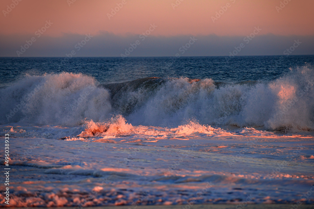 Beach sunrise over the tropical sea. Colorful sunset with wave splashes on the beach. Ocean waves background.
