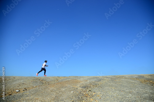 A man in a white shirt is jogging against a beautiful blue belly background.