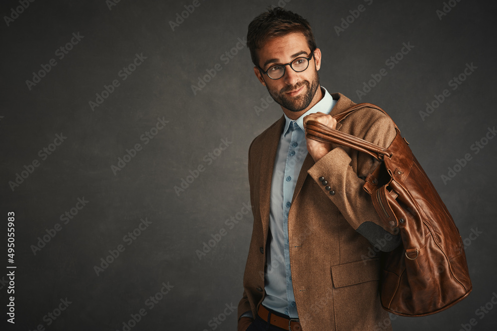 He makes that bag look good. Studio shot of a handsome young man posing against a gray background.