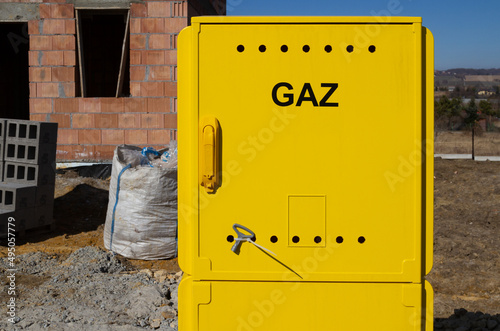 Yellow metal gas connection box at the construction site of a new single-family house. Unfinished stand-alone home building under construction. Letters in Polish language, Gaz means Gas.