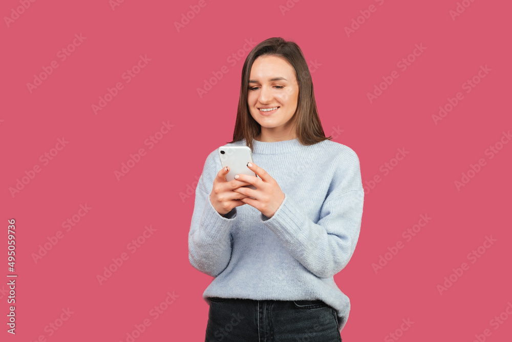 Positive young female is holding her phone and typing something. Positive young female is holding her phone and typing something.