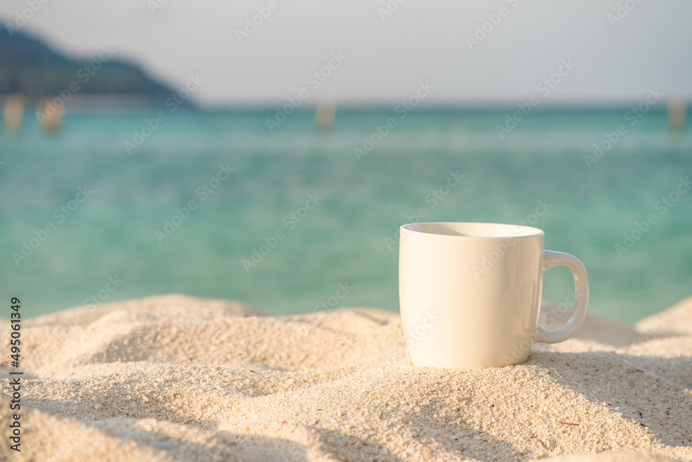 White coffee cup on white sand beach with blue sea background in morning. Coffee relaxation time in travel holiday concept. White coffee cup on white sand beach with blue sea background in morning. Coffee relaxation time in travel holiday concept.
