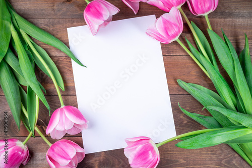 Fototapeta Naklejka Na Ścianę i Meble -  Pink white tulips and white sheet of paper on dark brown wooden background, horizontal, copy space, top view
