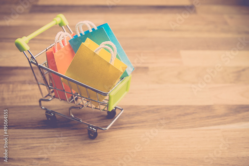 Model colorful shopping bags in trolley on wooden floor. Shopping at home or online internet shopping e-commerce idea concept.