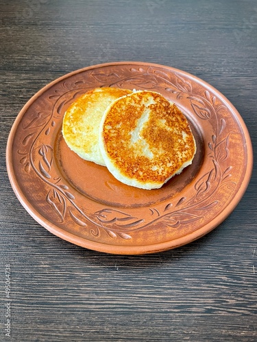 large vertical photo. homemade food. brown clay plate on a brown wooden table. top view close-up. two fried cheesecakes. healthy wholesome food. eco. bio. cottage cheese breakfast.