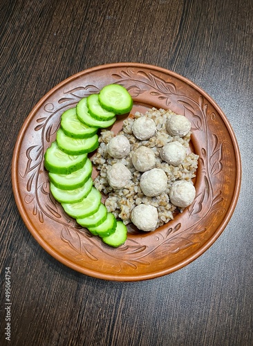 large vertical photo. homemade food. brown clay plate on a brown wooden table. top view close-up. buckwheat with chicken meatballs and cucumber slices. healthy wholesome food. eco. bio.