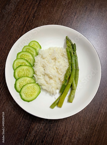 large vertical photo. dietary vegetarian food. basmati rice with vegetables. cucumber slices and asparagus on a round white plate. eco. healthy food.