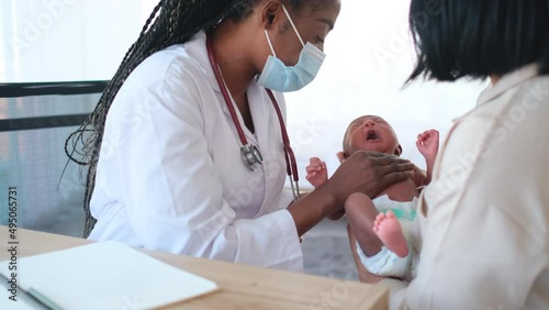 African American doctor with hygiene mask check and examination with newborn baby and discuss with mother for treatment.