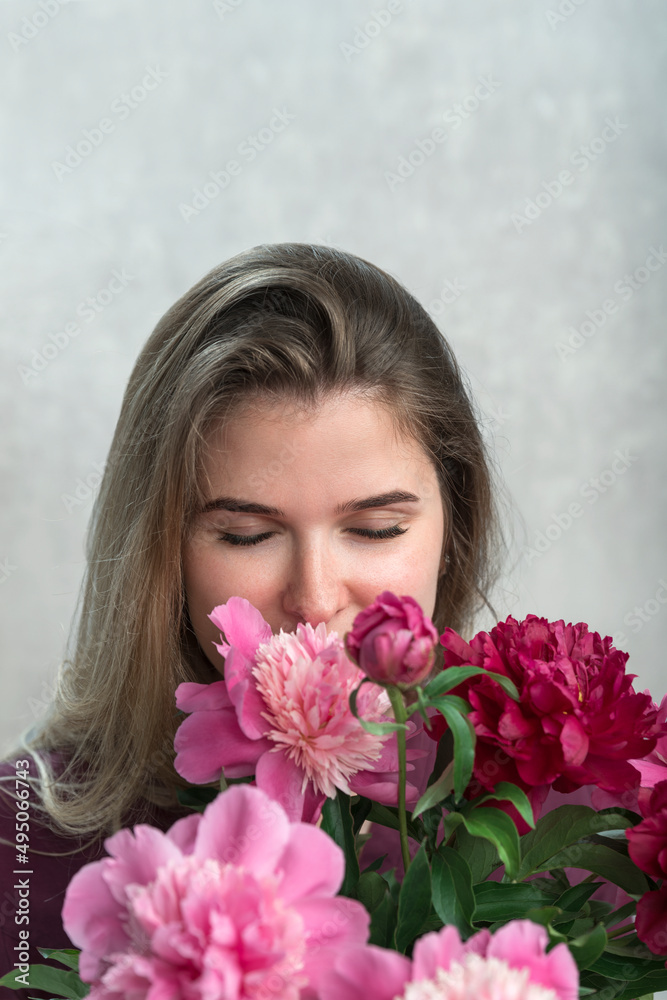 Attractive young woman with brown hair enjoys smell of peonies. Girl with natural beauty with bouquet of peonies. Vertical frame.