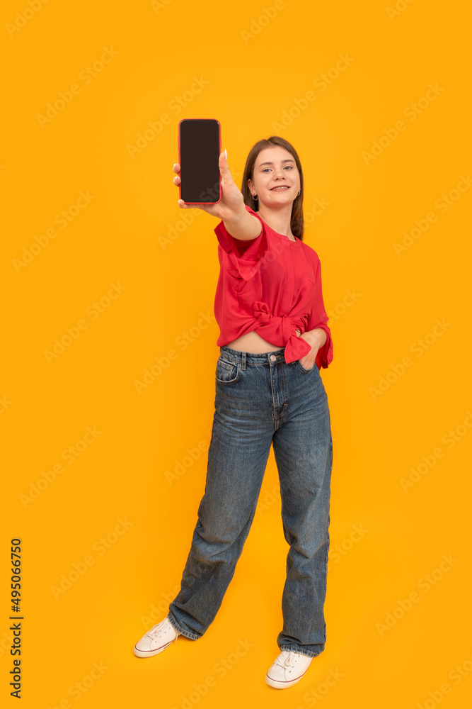 Young woman in red blouse holds phone with blank screen. Full-length portrait of girl with smartphone on yellow background. Mock up. Young woman in red blouse holds phone with blank screen. Full-length portrait of girl with smartphone on yellow background. Mock up.