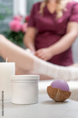 Scented candles and cosmetics on background beautician wraps body of woman with bandage. Cosmetic procedure.