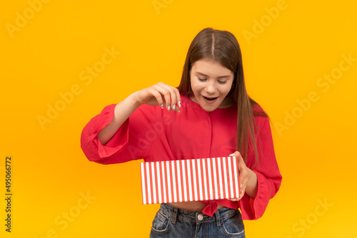 Surprised and delighted girl looks into an open gift box. Portrait of young brunette girl with gift in her hands.