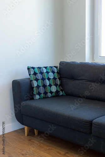Soft dark blue sofa by the window with a multi-colored pillow © HENADZI BUKA