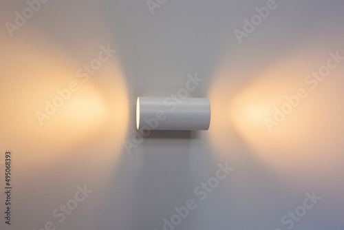 White wall lamp with switched on light on a white wall