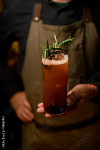 Close-up view of glass of signature cocktail decorated with rosemary on male bartender hand