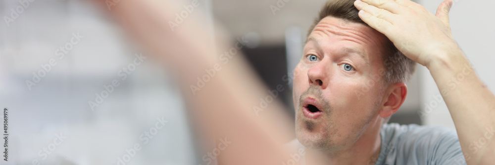 Naklejka premium Unshaven man looks in the mirror and straightens his hair