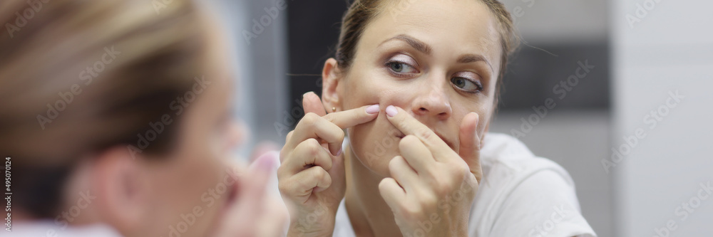 Young woman looks in the mirror and squeezes out a pimple Young woman looks in the mirror and squeezes out a pimple