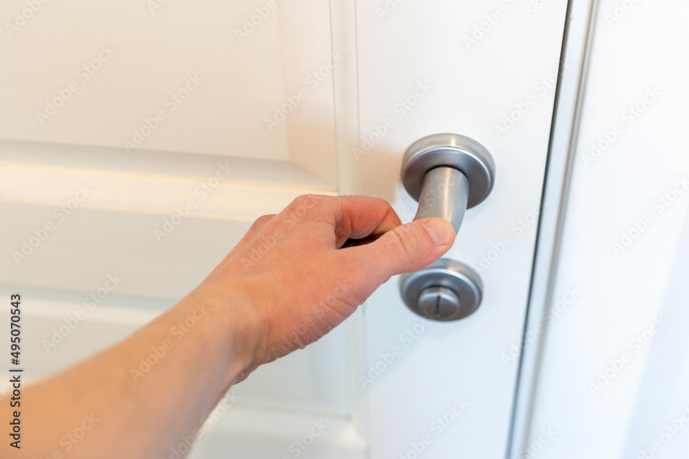 Hand presses the doorknob of a white door Hand presses the doorknob of a white door