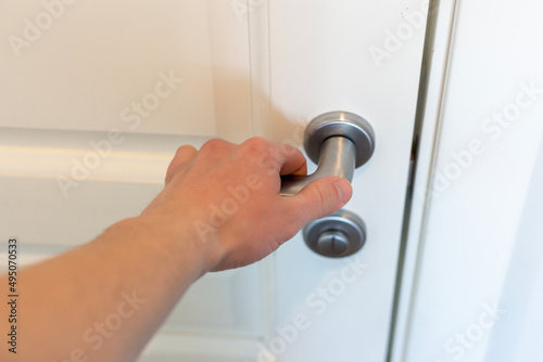 Hand presses the doorknob of a white door